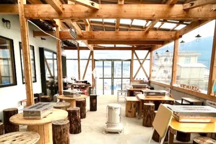 木の柱と梁の小屋の中に、焼き台をのせた丸いテーブルと丸太のいすが並ぶ